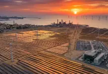 MoU Inked on 500 MW Green Hydrogen Capacity in Alexandria Sunset over a coastal solar farm with wind turbines and offshore wind farms in the distance, beside an industrial plant.