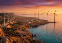 Solar Power and Green Hydrogen Opportunity in Libya Coastal wind farm at sunset with tall turbines along the rocky shore and nearby buildings by the water.