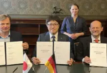 JDA on Liquefied Hydrogen Supply Chain to Europe from Japan Three executives sign a Joint Development Agreement at a formal signing ceremony, with Japan and Germany flags on the table and a woman standing behind them.