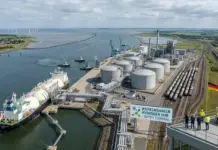 MoU To Develop LOHC-Based Hydrogen Import Path in Germany Industrial port scene with large cylindrical storage tanks, pipelines, cranes, and a docked ship at Wilhelmshaven Hydrogen Hub Import Terminal.