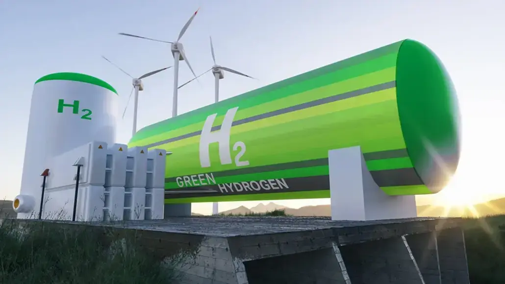 Large green hydrogen storage tank and tanker labeled H2, with wind turbines in the background at sunset/bright sky.