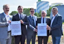$33m For Hydrogen Pipeline and Storage Projects for Chemnitz Five men in suits stand outdoors, holding two large certificates showing 20,720,000 euros and 9,615,000 euros, with solar panels and storage tanks in the background.