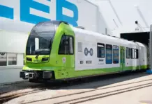 World-First Hydrogen-Powered Train for Narrow-Gauge Green and white passenger tram at a maintenance depot, entering a service bay on tracks.