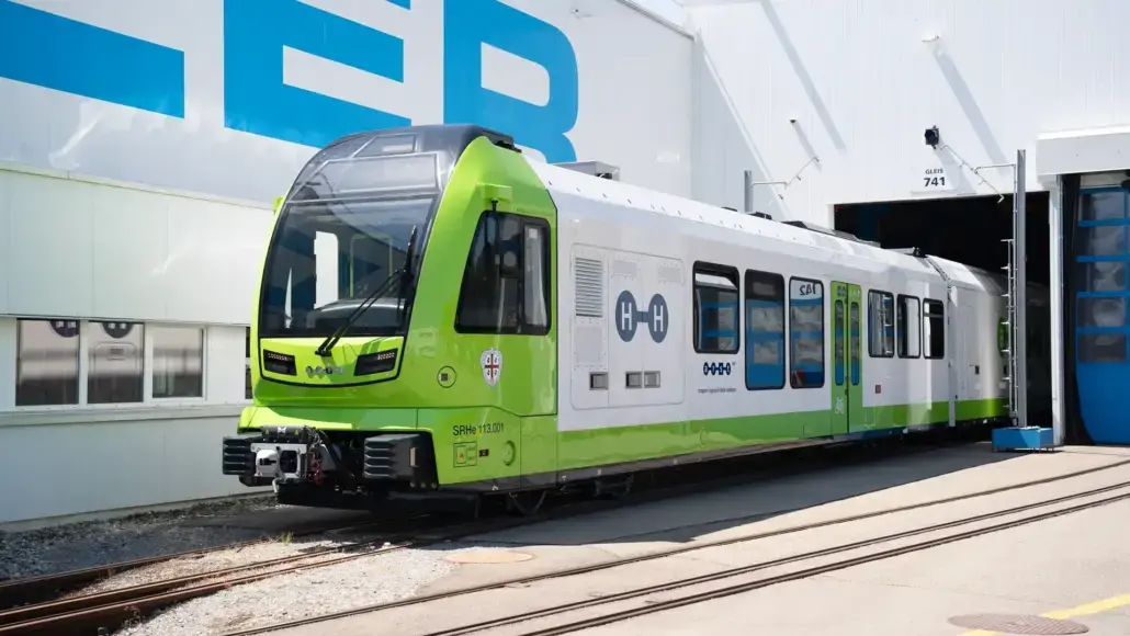 Green and white passenger tram at a maintenance depot, entering a service bay on tracks.