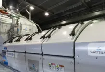 Wartsila Tests Mega 100% Hydrogen Engine on Spain Grid Large white industrial module labeled Wärtsilä with hydrogen markings, pipes and controls in a high-tech facility floor.