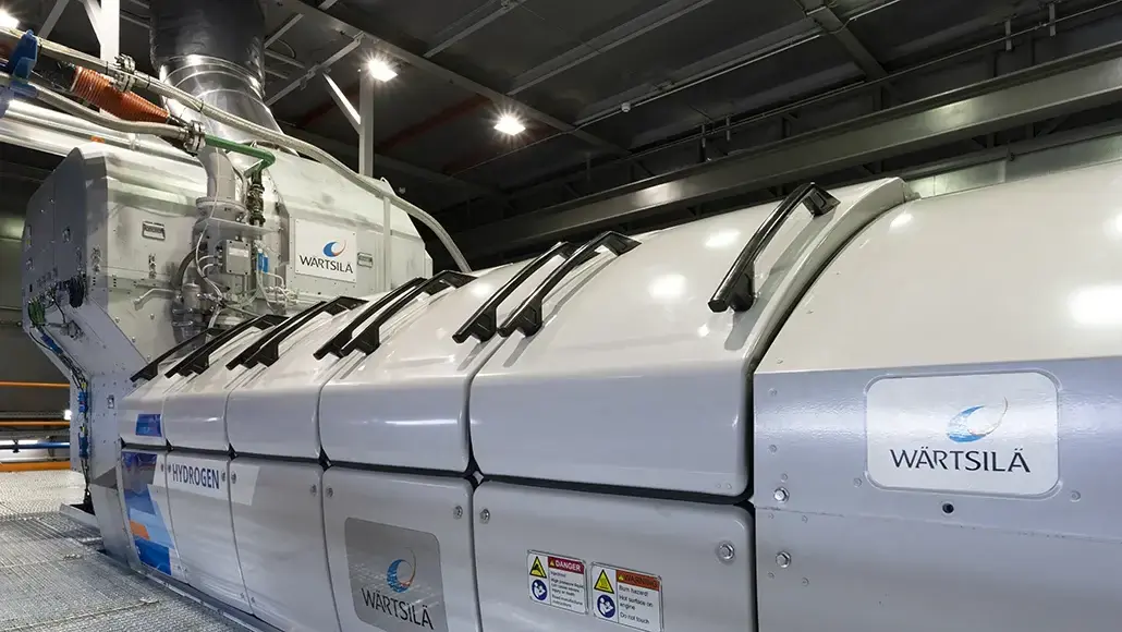Large white industrial module labeled Wärtsilä with hydrogen markings, pipes and controls in a high-tech facility floor.