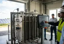 AI Optimizing Electrolyzer Performance for Green Hydrogen Group of engineers in safety gear inspecting a large industrial machine with a rugged touchscreen monitor showing data.