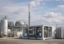 Nordenham Innovation Center Commissions New Hydrogen Plant Industrial processing facility with large stainless tanks, complex piping, and a tall smokestack against a blue sky.